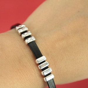 May include: A black leather bracelet with silver rectangular beads.
