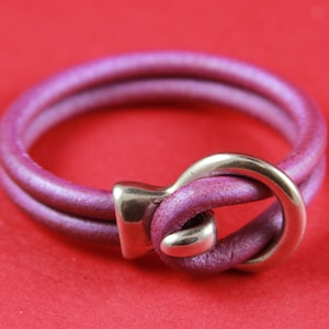 May include: A double-strand leather bracelet with a silver clasp. The bracelet is a deep purple color.