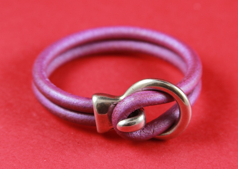 K&ouml;nnte beinhalten: Ein doppelschichtiges Lederarmband mit einem silbernen Verschluss. Das Armband ist dunkelviolett.