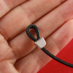 May include: A black leather cord with a silver metal clasp. The cord is looped and held in a hand.