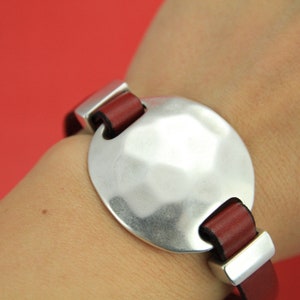 May include: A silver bracelet with a large, round, hammered metal charm and a brown leather strap.
