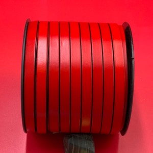 May include: A spool of red leather cord with black edges. The cord is wound tightly around a black plastic spool.