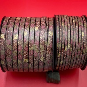 May include: A roll of brown and gold patterned ribbon with a floral design. The ribbon is wound around a spool.