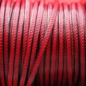 May include: A spool of red leather cord with a decorative pattern. The cord is wound tightly around the spool.