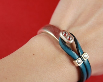 Könnte beinhalten: Ein türkisfarbenes Lederarmband mit silbernen Akzenten und klaren Kristallverzierungen. Das Armband ist um das Handgelenk einer Person gewickelt.