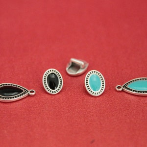 May include: Four silver-toned metal charms with black and turquoise enamel. Two charms are oval shaped and two are teardrop shaped.