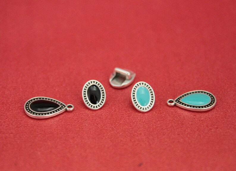 May include: Four silver-toned metal charms with black and turquoise enamel. Two charms are oval shaped and two are teardrop shaped.