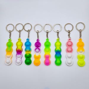 May include: Eight colourful bubble-popping fidget toy keyrings. Each keyring features a different gradient of colours, including yellow, pink, blue, and green. The keyrings are made of silicone and have a metal ring.