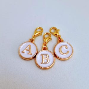 May include: Three gold-toned metal charms with white enamel circles and gold letters A, B, and C. The charms have a spring-loaded clasp.