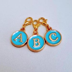 May include: Three gold-coloured charms with blue enamel circles and white letters spelling out "ABC". Each charm has a gold-coloured lobster clasp.