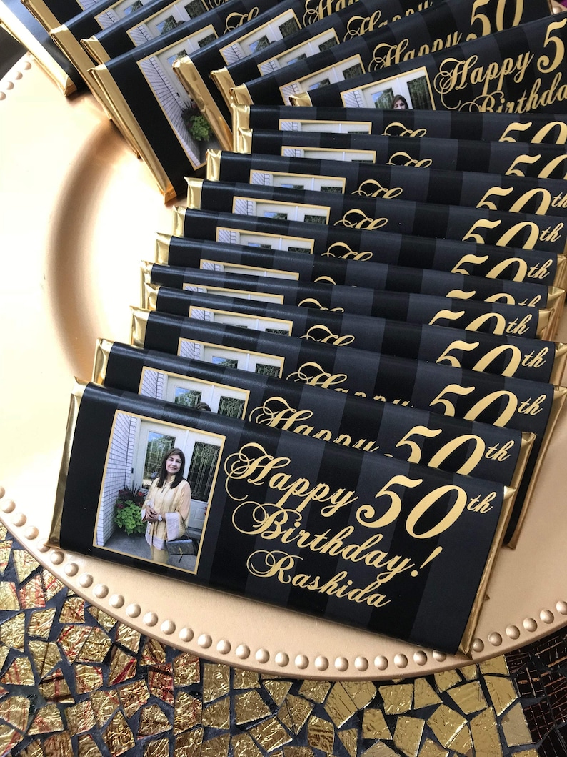 May include: A stack of black and gold chocolate bars with a photo of a woman and the text "Happy 50th Birthday! Rashida" printed on the front.