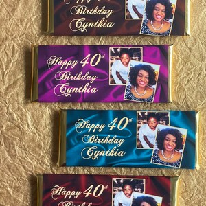 Puede incluir: Cuatro envoltorios de barritas de chocolate con detalles en l&aacute;mina dorada. Cada envoltorio presenta un fondo de color diferente con textura satinada. Los envoltorios tienen el texto "Happy 40th Birthday Cynthia" y una foto de una mujer y un ni&ntilde;o.