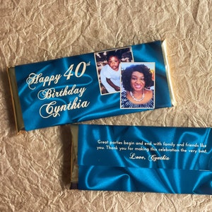 Puede incluir: Una barra de chocolate azul y dorada con una foto de una mujer y un ni&ntilde;o en el frente. El texto "Happy 40th Birthday Cynthia" est&aacute; impreso en el frente de la barra. La parte posterior de la barra tiene un fondo de sat&eacute;n azul con el texto "Great parties begin and end with family and friends like you. Thank you for making this celebration the very best. Love, Cynthia."