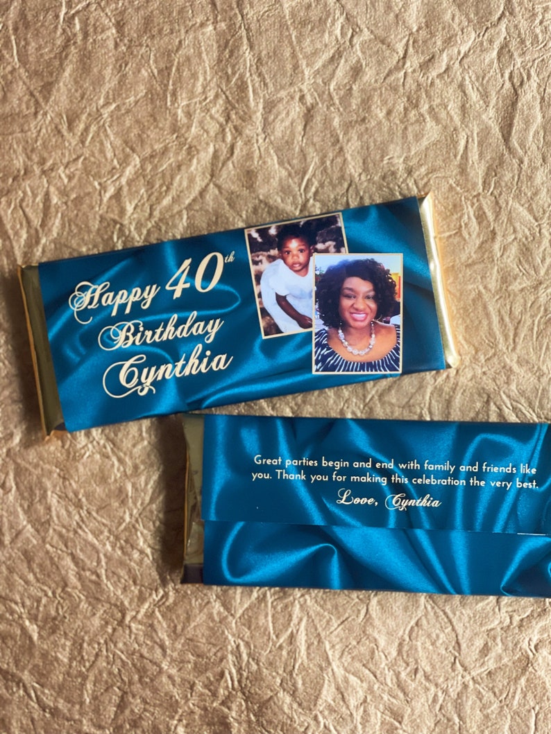 Puede incluir: Una barra de chocolate azul y dorada con una foto de una mujer y un ni&ntilde;o en el frente. El texto "Happy 40th Birthday Cynthia" est&aacute; impreso en el frente de la barra. La parte posterior de la barra tiene un fondo de sat&eacute;n azul con el texto "Great parties begin and end with family and friends like you. Thank you for making this celebration the very best. Love, Cynthia."
