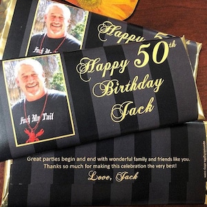 May include: A black and gold chocolate bar with a striped pattern. The bar has a photo of a man and the text "Happy 50th Birthday Jack". The back of the bar has the text "Great parties begin and end with wonderful family and friends like you. Thanks so much for making this celebration the very best! Love, Jack".