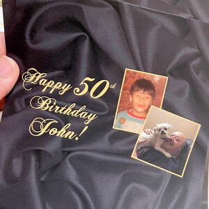 Puede incluir: Una tarjeta negra con una inscripci&oacute;n dorada que dice "Happy 50th Birthday John!" La tarjeta tiene dos fotos, una de un ni&ntilde;o peque&ntilde;o y otra de un hombre mayor con un perro.