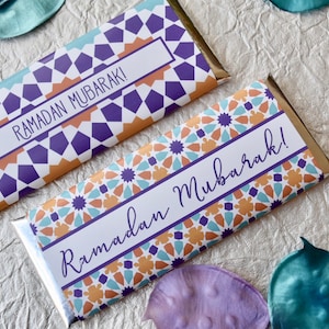 May include: Two chocolate bar wrappers with a geometric pattern in shades of orange, blue, and purple. The wrappers have the text "Ramadan Mubarak!" printed on them.