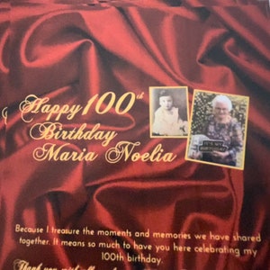 Puede incluir: Un fondo de sat&eacute;n rojo con letras doradas que dicen "Happy 100th Birthday Maria Noelia". Hay dos fotos de una mujer, una de ni&ntilde;a y otra de adulta mayor. El texto debajo de las fotos dice "Porque atesoro los momentos y los recuerdos que hemos compartido juntos. Significa mucho para m&iacute; tenerte aqu&iacute; celebrando mi cumplea&ntilde;os n&uacute;mero 100."