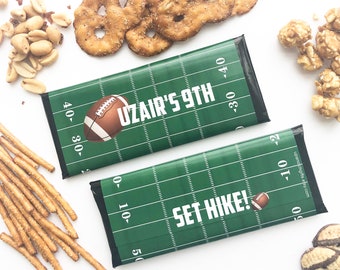 May include: Two green and white football-themed chocolate bar wrappers with the text "Uzair's 9th" and "Set Hike!" printed on them. The wrappers feature a football field design with yard lines and a brown football.