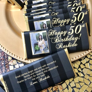 May include: A stack of black and gold chocolate bar wrappers with a photo of a woman and the text "Happy 50th Birthday! Rashida" and "Great parties begin and end with wonderful family and friends like you. Thanks so much for making this celebration the very best! Love, Rashida".
