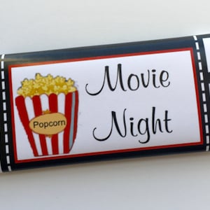 Puede incluir: Un envoltorio de barra de chocolate rojo, blanco y negro con un diseño de tira de película. El envoltorio tiene una imagen de un cubo de palomitas de maíz y el texto "Noche de cine".