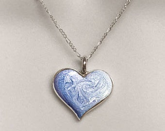 May include: A silver necklace with a blue heart pendant. The heart has a delicate white design on it. The necklace is on a white background with the text "Memorial Silver" above it.