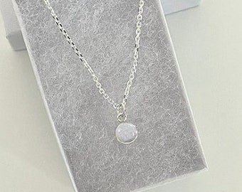 May include: A silver chain necklace with a 6mm moonstone pendant. The necklace is in a small gray box with the text "HEAVEN STONES® from Memorial Silver" on the lid. The text "6mm Sterling Silver" and "Heaven Stone Color: MOONSTONE" are printed below the box.
