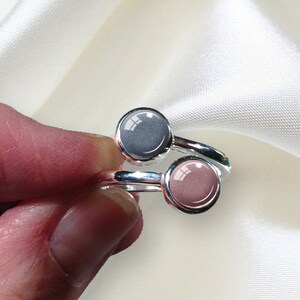 May include: Two silver rings with round, cabochon stones. The top ring has a gray stone, and the bottom ring has a pink stone.