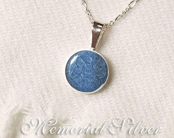 May include: A silver chain necklace with a blue pendant featuring a swirling pattern. The pendant is round and has a smooth, polished finish.