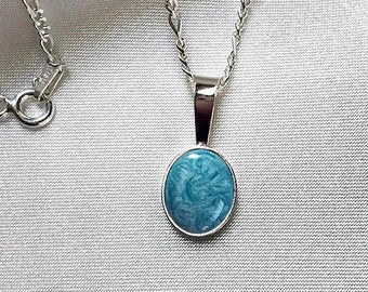 May include: A silver chain necklace with a pendant featuring a round, light blue cabochon stone.