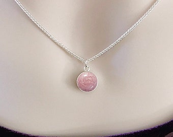 May include: A silver chain necklace with a small, round pendant. The pendant is made of silver and has a pink, speckled surface. The text "HEAVEN STONES® from Memorial Silver" is visible at the top of the image.