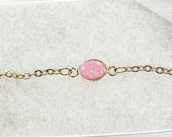 May include: A delicate gold chain bracelet with a single pink oval-shaped gemstone.