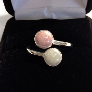 May include: A silver ring with two round stones, one pink and one white, set in a twist design. The ring is in a black velvet box.