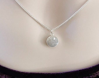May include: A silver chain necklace with a round pendant containing a gray cremation ash memorial. The pendant is attached to a silver chain. The text "HEAVEN STONES® from Memorial Silver" is visible at the top of the image.