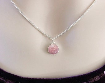 May include: A silver chain necklace with a pink round pendant. The pendant is made of memorial silver and has a textured surface. The text "HEAVEN STONES® from Memorial Silver" is displayed above the necklace.