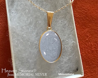 May include: A gold chain necklace with an oval-shaped pendant featuring a moonstone. The pendant is set in a gold frame and the chain has a lobster clasp. The necklace is in a white box with the text "Heaven Stones® from MEMORIAL SILVER Moonstone".