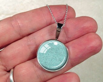 May include: A silver chain necklace with a round pendant. The pendant is filled with light blue sand.