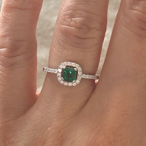 May include: A silver ring with a square emerald green gemstone surrounded by a halo of smaller clear gemstones.