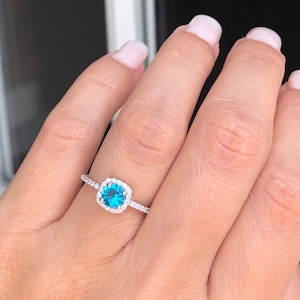 May include: A silver ring with a blue gemstone surrounded by smaller white gemstones.