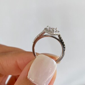 May include: A silver ring with a large, clear, oval-shaped gemstone surrounded by smaller gemstones. The ring has a delicate, twisted band.