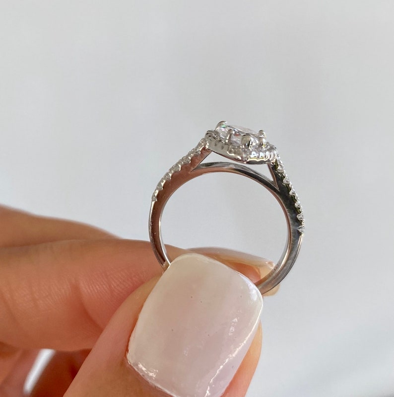 May include: A silver ring with a large, clear, oval-shaped gemstone surrounded by smaller gemstones. The ring has a delicate, twisted band.