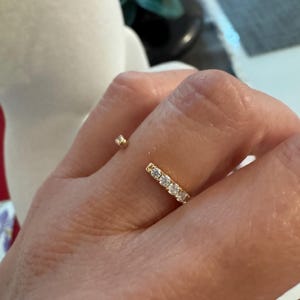 May include: A gold open-style ring featuring a row of five small, clear, round-cut stones on one end and a single, solitary, clear, round-cut stone on the opposite end, creating a delicate and balanced appearance on the finger.