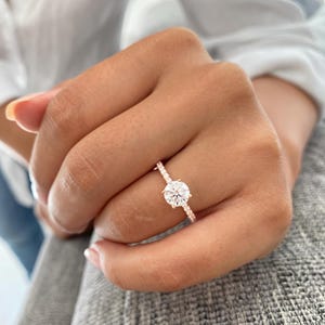 May include: A rose gold engagement ring with a round brilliant cut diamond center stone and a pave diamond band.