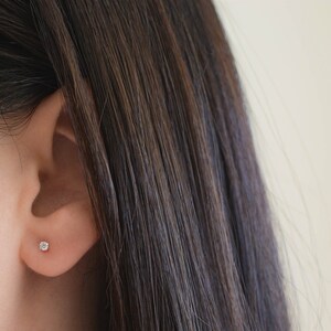May include: A close-up of a person's ear with a small, round, clear diamond stud earring.