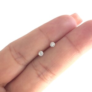 May include: A pair of small, round, clear diamond stud earrings set in gold.