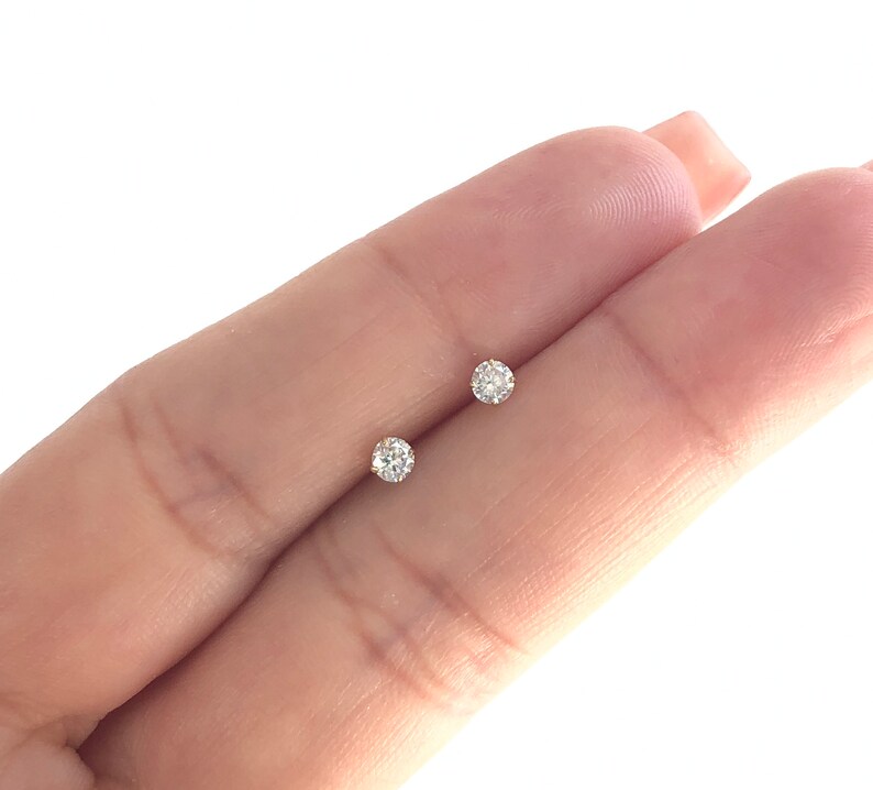 May include: A pair of small, round, clear diamond stud earrings set in gold.
