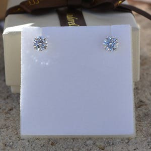 May include: Two small, round, clear diamond earrings on a white background.