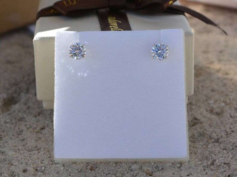 May include: Two small, round, clear diamond earrings on a white background.