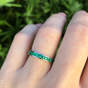 May include: A silver band ring with a row of emerald green gemstones.