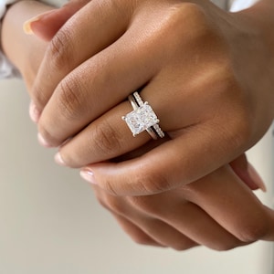 Puede incluir: Primer plano de una mano de mujer con un anillo de plata con un gran diamante rectangular transparente. El anillo está engastado con diamantes más pequeños en la banda.